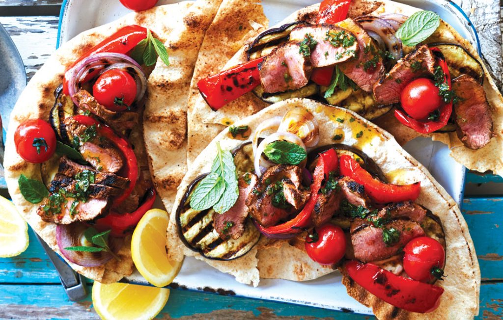 Flatbread filled with lamb, red peppers, tomatoes and mint on a blue table