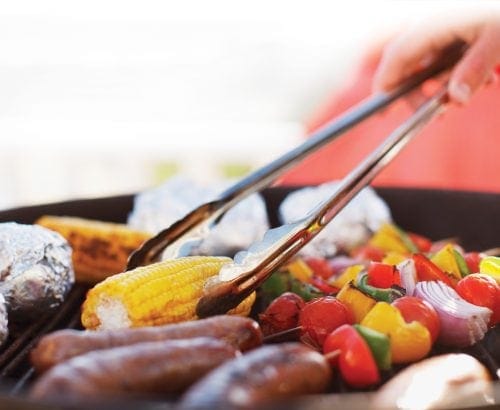 Barbecuing sausages, corn and vegetable kebabs