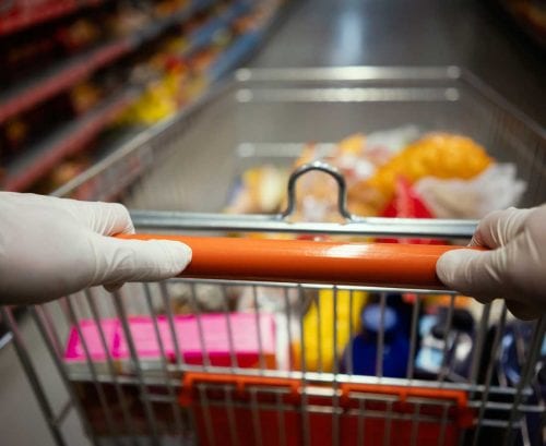person wearing gloves pushing supermarket trolley