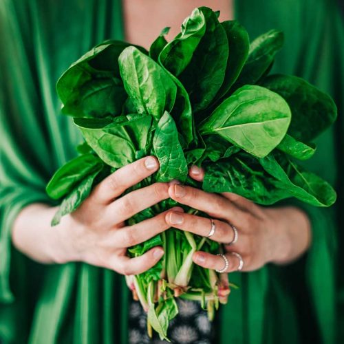 Woman in green holding a bunch of spinach