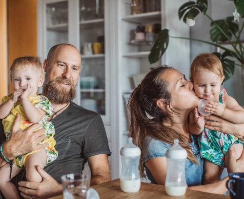 Dad, mum and two babies at kitchen table with bottles