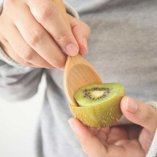 Person scooping out a kiwifruit