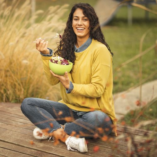 Woman eating a plant-based meal, sitting crossed legged outside