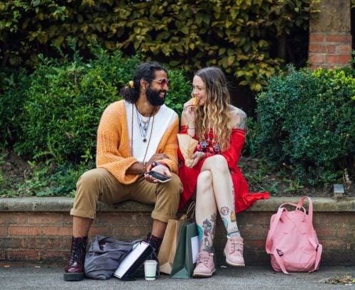Hippy couple sitting on a ledge outside eating lunch