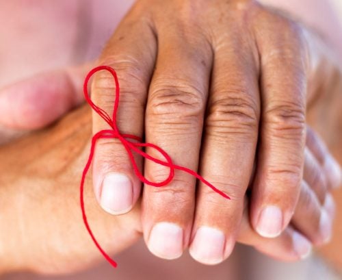 Older person's hand with a bow tied around a finger to remind them not to forget