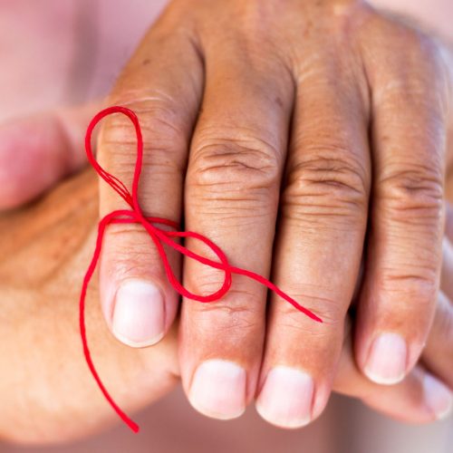 Older person's hand with a bow tied around a finger to remind them not to forget