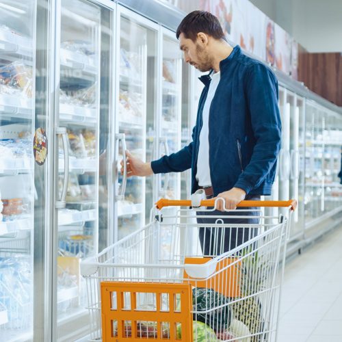 Man choosing frozen meal in supermarket freezer