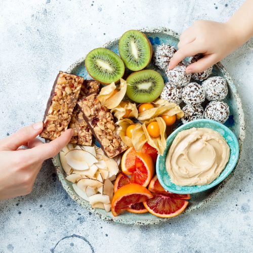 two hand reaching for an array of healthy snacks on a plate
