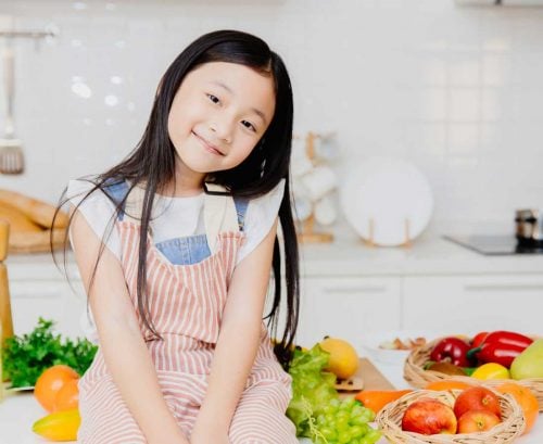 Cute kid sitting on bench surrounded by vegetables