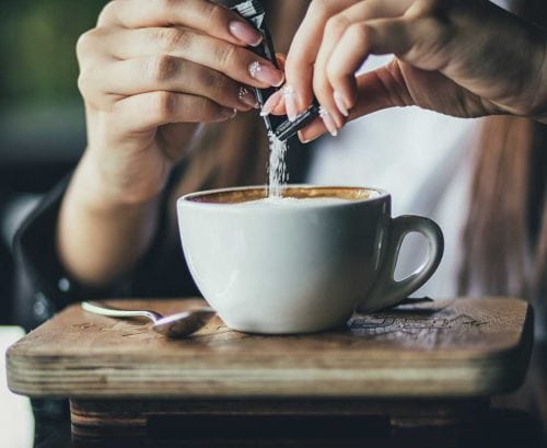 Woman pouring sugar sachet into her coffee