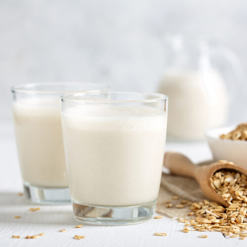 Two glasses of oat milk next to a scoop of oats
