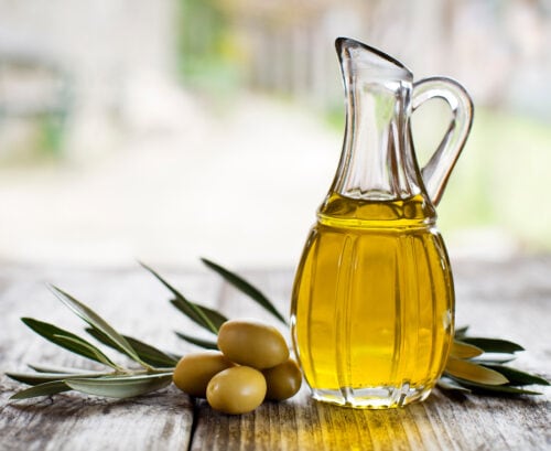 A glass jug of extra virgin olive oil with an olive branch and a few olives