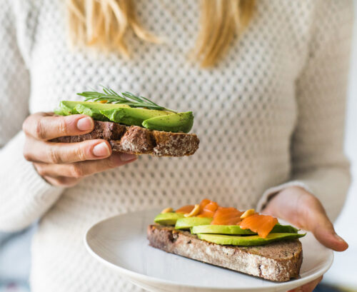 Woman holding out avocado on toast with various toppings