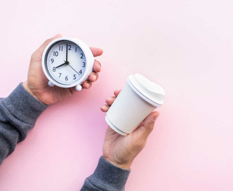 Hands holding alarm clock and takeaway coffee cup